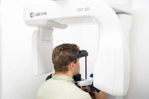 Dental professional positioning patient for 3D panoramic X-ray scan using DEXIS OP 3D imaging machine in modern dental office